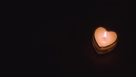 hand putting romantic lit heart shaped white candle onto black background