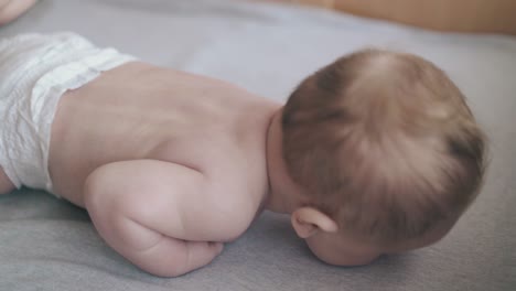 cute fair haired newborn boy lies on baby table and cries