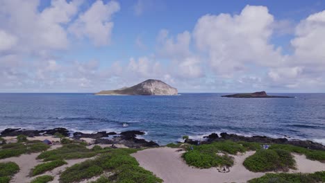 Toma-Estacionaria-De-Dos-Pequeñas-Islas-De-Formación-Volcánica-Frente-A-La-Costa-De-Oahu-Hawaii-En-El-Océano-Pacífico-Con-Playa-De-Arena-Con-Vegetación-En-Primer-Plano