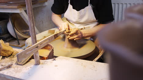 close up of male potter shaping clay for pot on pottery wheel in ceramics studio