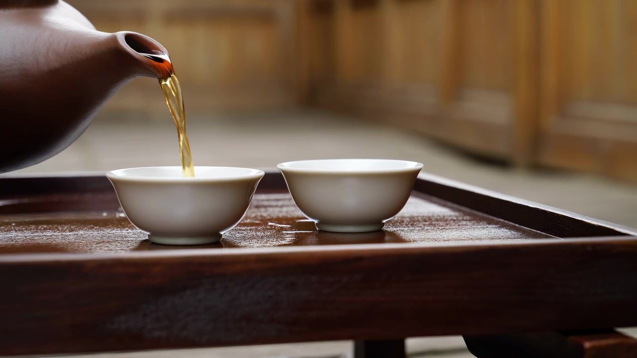 木製のトレイに乗った二つの磁器のカップ。土瓶から穏やかな琥珀色の紅茶が注がれ、暖色系の色合いが広がるミニマリストなティータイム。