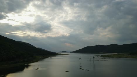 aerial reverse footage of this fantastic landscape of the lake with rainclouds, sun setting, palm trees in the middle of the lake; saraburi, thailand
