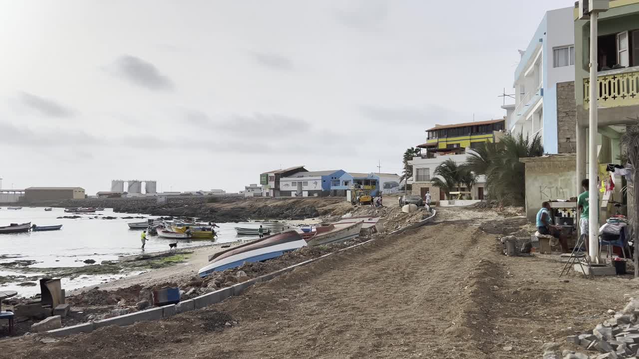 Coastal view in Sal Rei, Cape Verde, shows colorful boats along the shore, local buildings, and people working near the water. Captures the charm of daily life in this island community