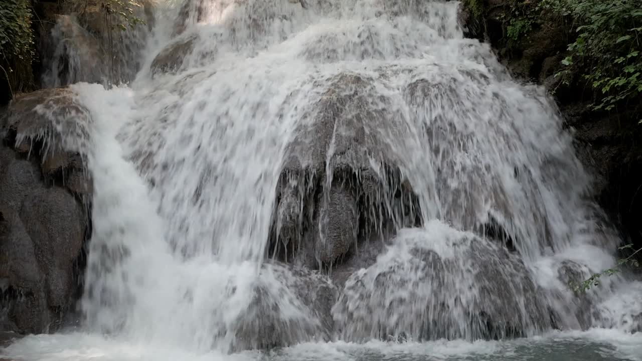 Closeup of water cascade on rocks. River stream drops on different levels of bedrock onto water pool. Leaves from vegetation on the sides