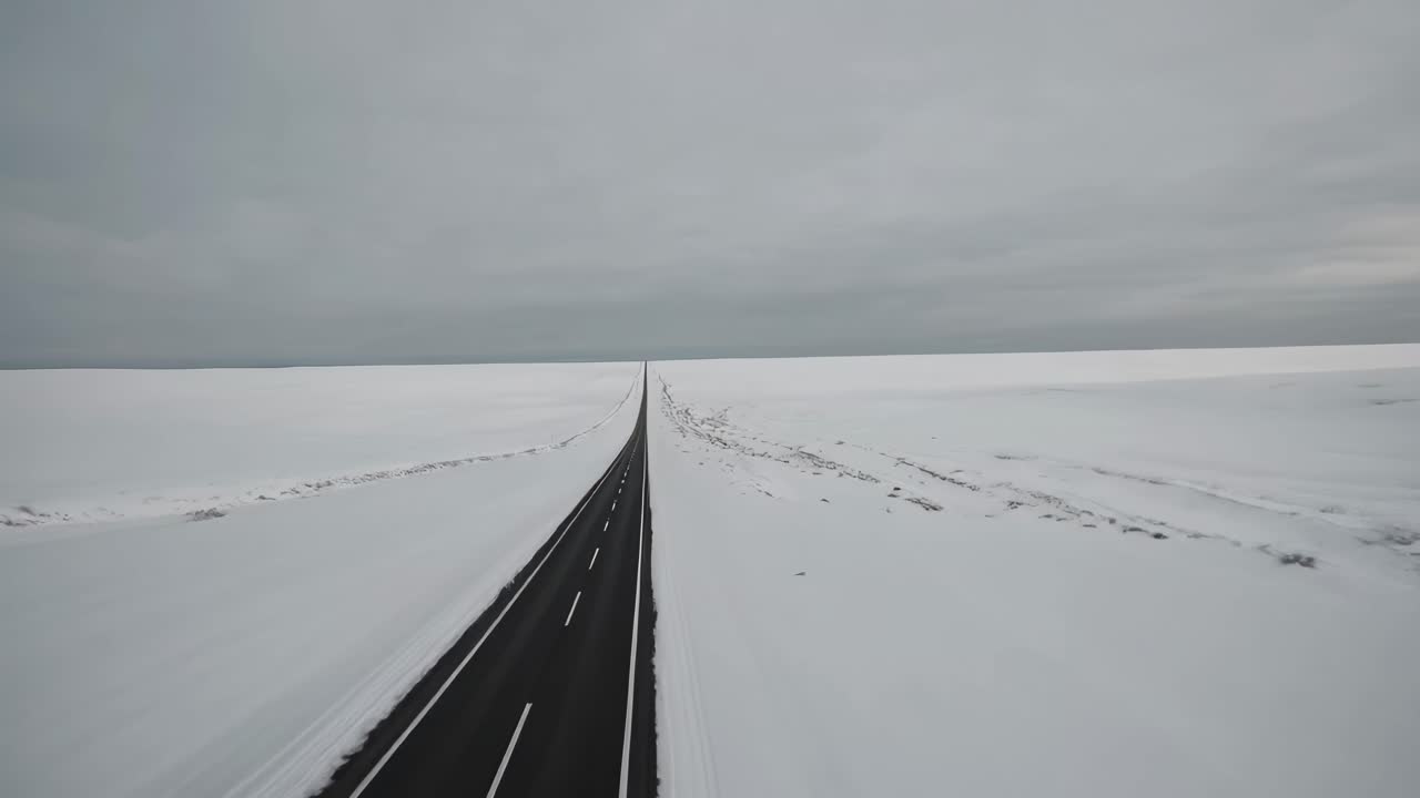 Aerial video shot of a straight road cutting through a vast snowy landscape, emphasizing isolation