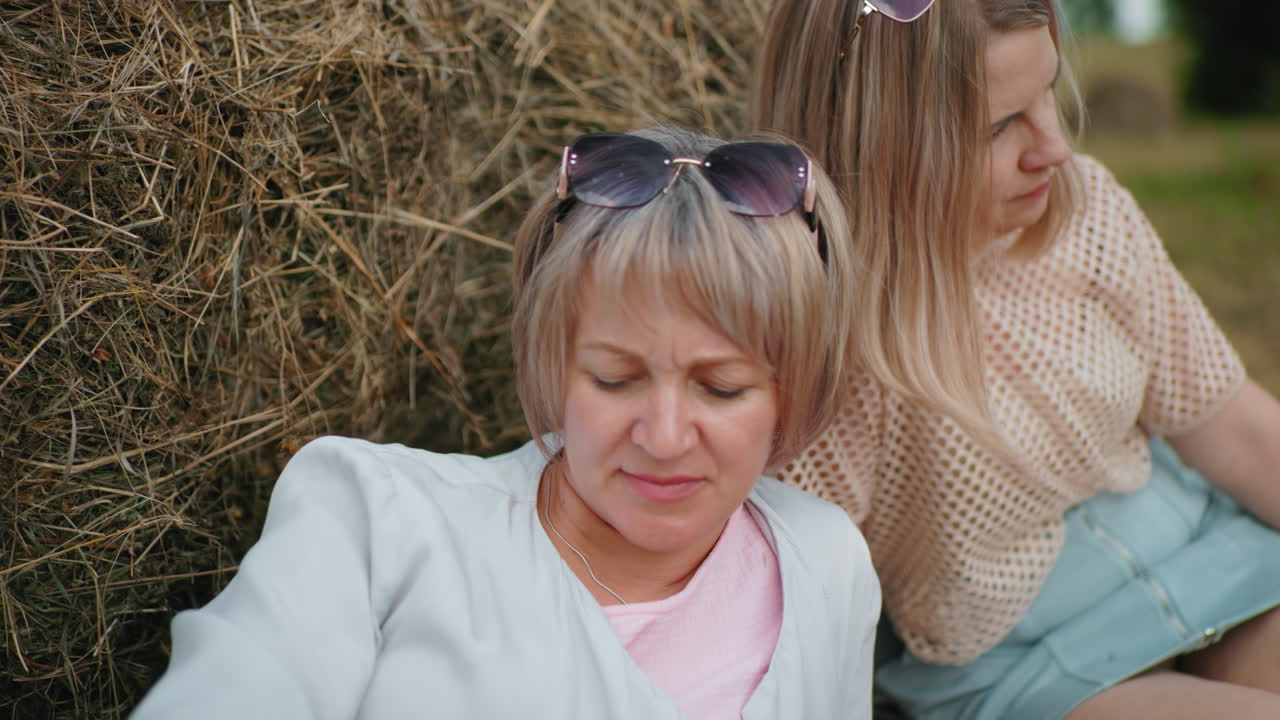 평화로운 야외 순간을 즐기는 자매, 머리에 선글라스를 착용하여  에 편안하게, 조용한 시골 설정은 자연 시골 풍경에서 따뜻함, 평온함, 그리고 형제자매의 유대를 포착합니다.