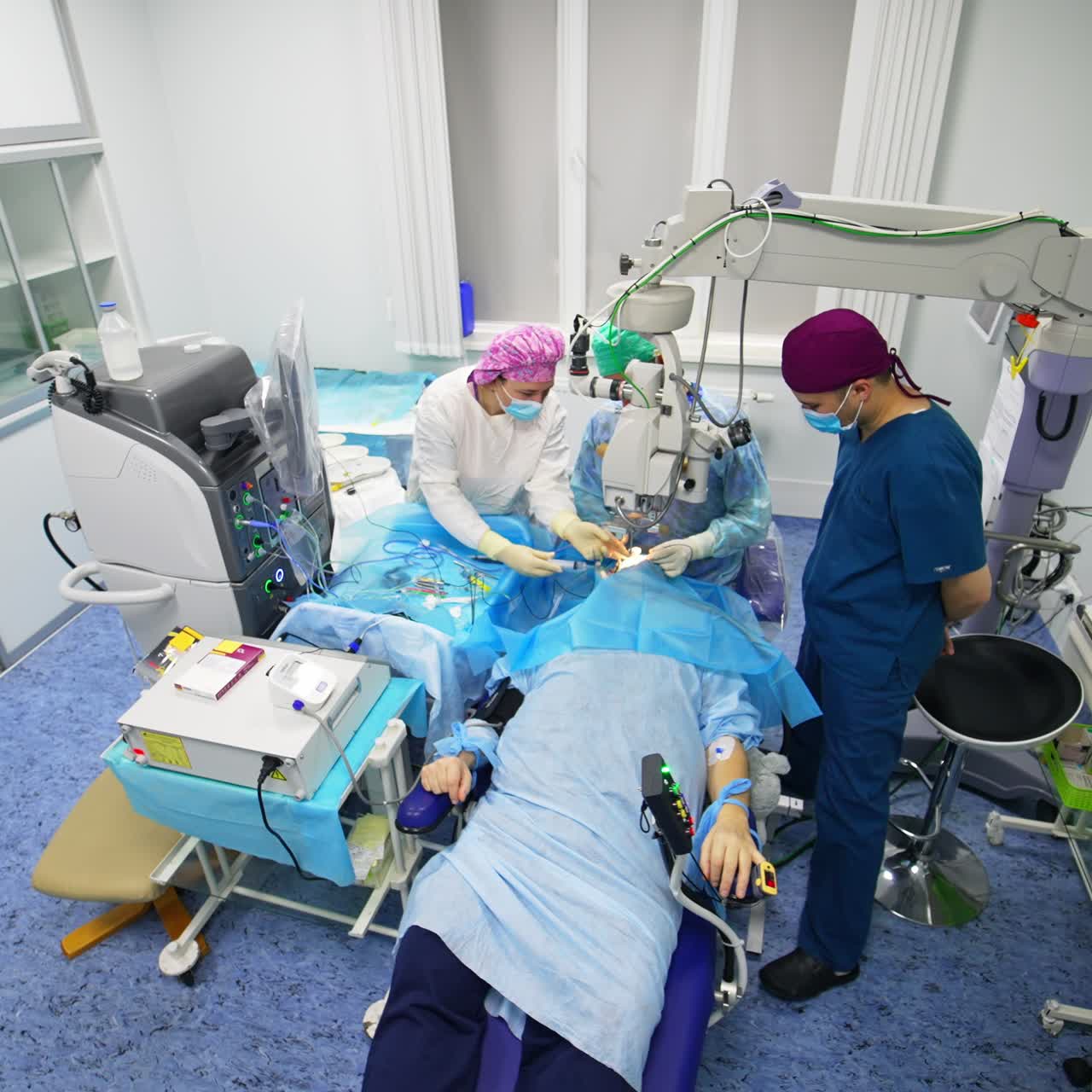 Eye surgery performed at modern operational theatre. Chief surgeon uses tools holding them in both hands and looks into binoculars. High angle view