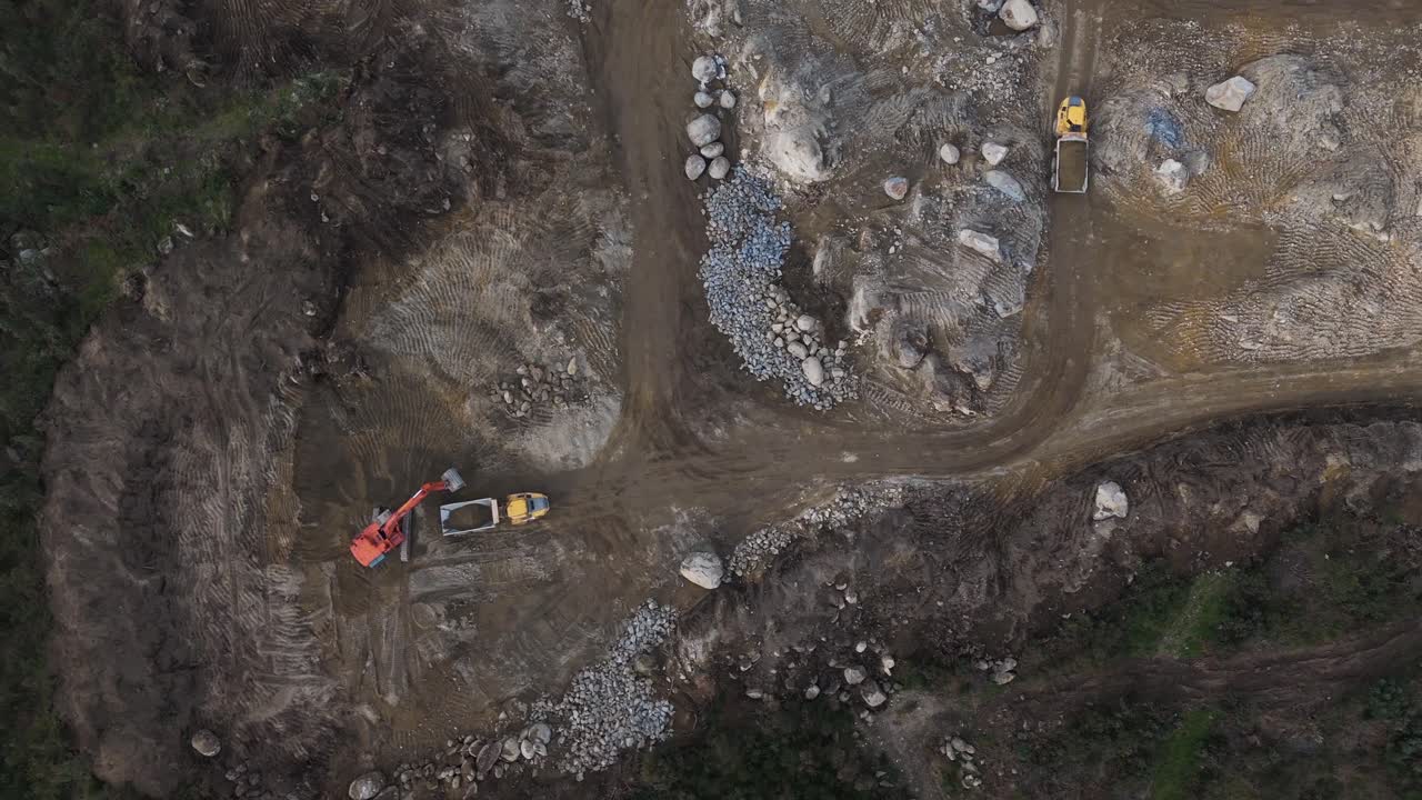 Aerial excavator loading sand into truck on wide rocky site in Portugal