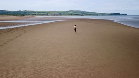 Aerial-footage-of-young-man-without-shirt-and-barefoot-running-on-beach