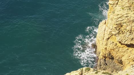 Ocean-waves-break-against-high-sea-cliffs-on-rocky-coastline-of-Mediterranean,-slow-motion-zoom