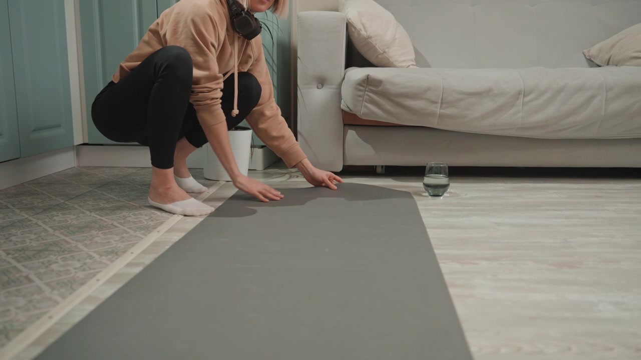 Woman practices yoga. Relaxing yoga routine in cozy living room. Caucasian woman preparing for morning yoga on soft surface. Calm woman unrolls mat in warm living room to start wellness routine