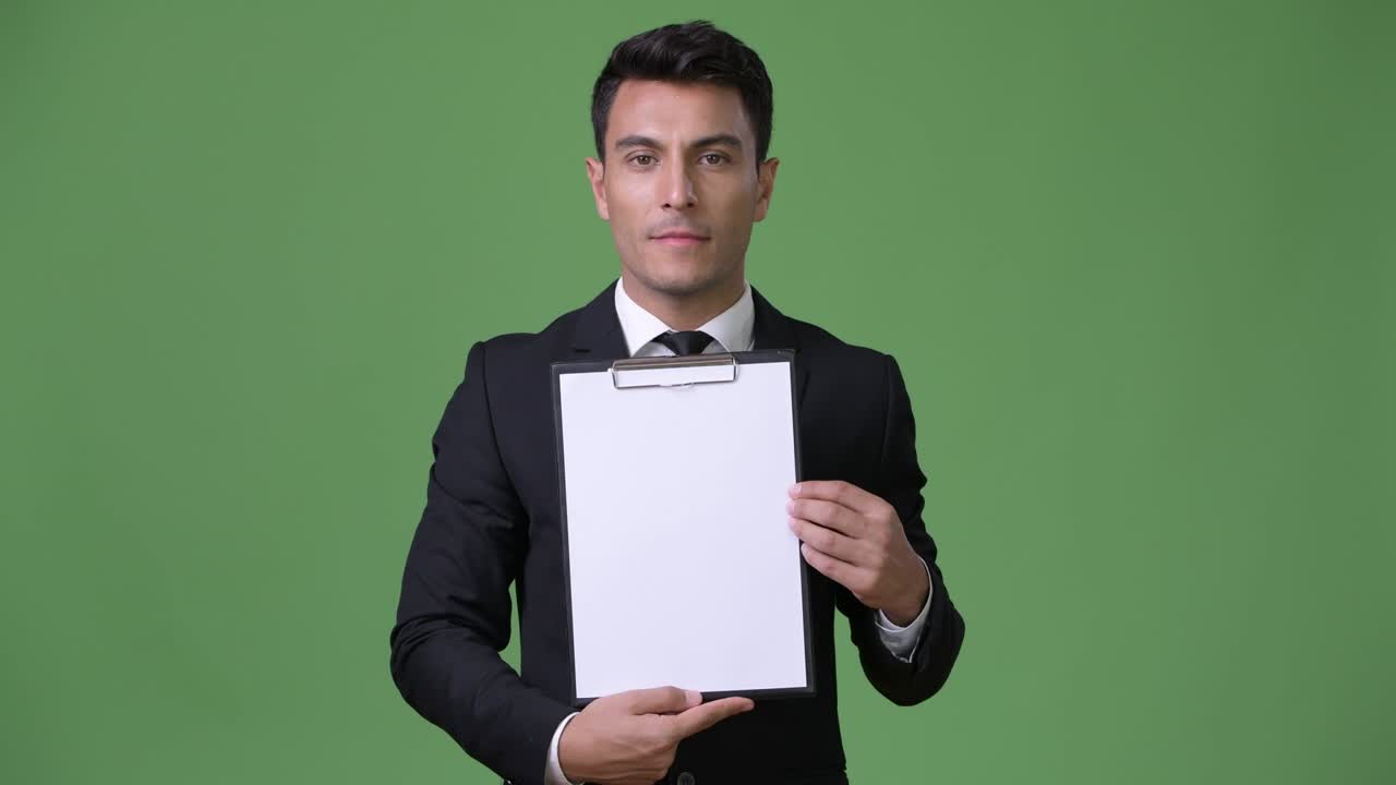Young handsome Hispanic businessman against green background