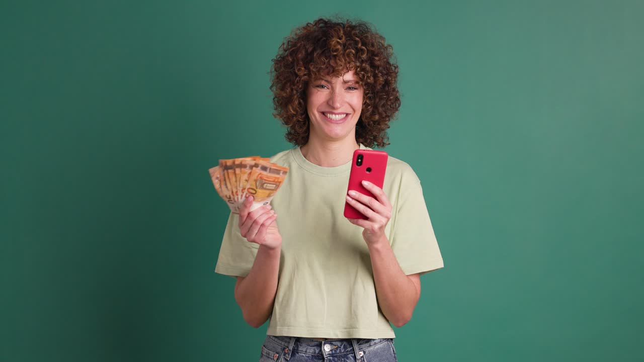 Excited woman with cash and mobile phone in green studio
