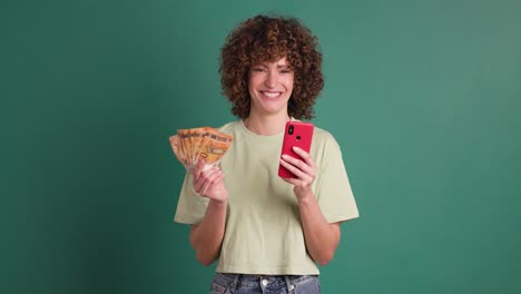 excited woman with cash and mobile phone in green studio