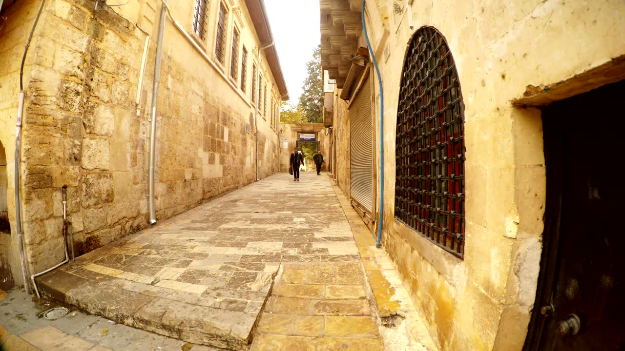 Mujer musulmana con un niño y un hombre con maletín caminan por una calle antigua, estrecha y empedrada de Urfa