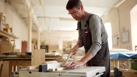 medium shot of mature carpenter using circular saw for cutting pieces of wood in his woodworking workshop