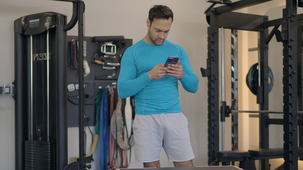 retrato de un hombre en forma francés dentro del gimnasio usando un teléfono móvil