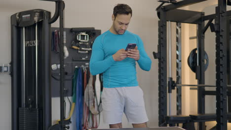 Portrait-Of-A-French-Fit-Man-Inside-The-Gym-Using-Mobile-Phone