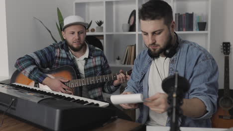 jóvenes músicos masculinos creando, tocando guitarra y teclado eléctrico en casa