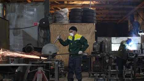 workers working with metal construction on plant. metal processing with big angle grinder disk saw and welder welding. sparks in metalworking at factory.