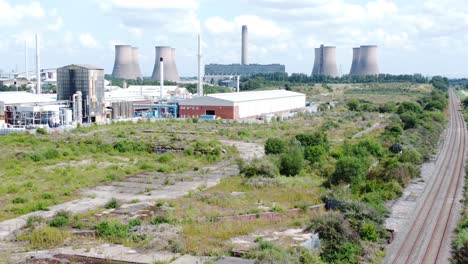 Industrial-warehouse-power-plant-refinery-buildings-under-smokestack-wasteland-aerial-view-reverse-descending-over-rail-tracks