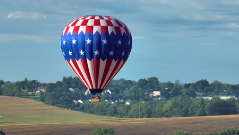 un globo aerostático con bandera estadounidense se eleva sobre las tierras de cultivo rurales del condado de lancaster, pensilvania, ee.uu.