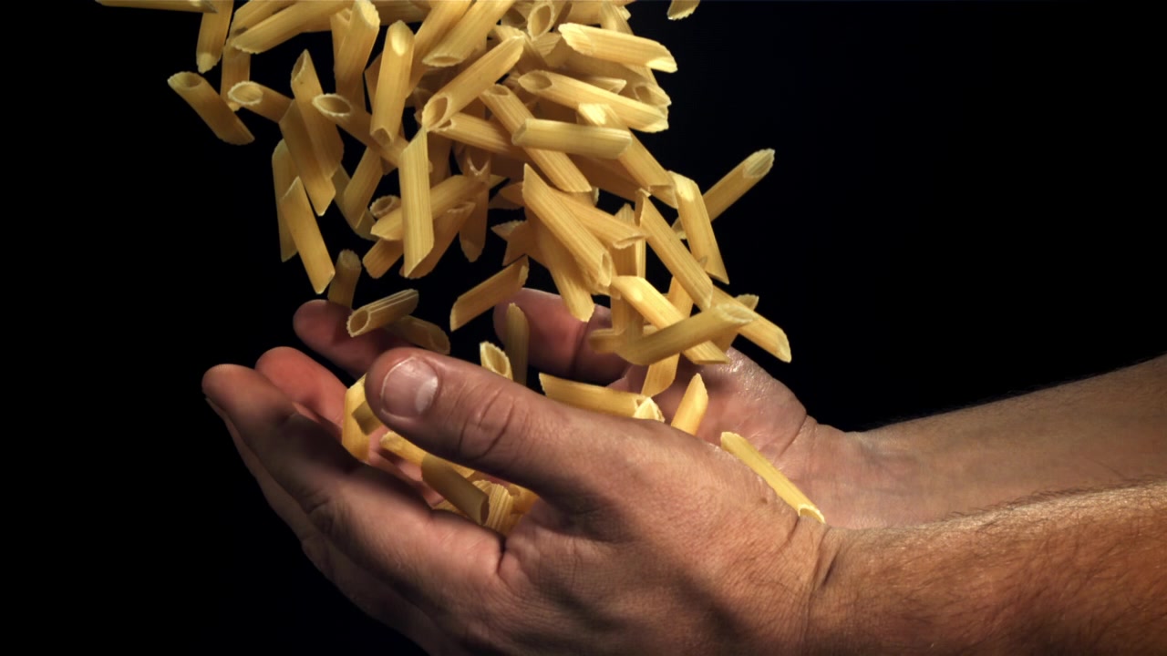 Pasta penne secca che cade dalle mani al rallentatore