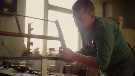 Focused-man-working-with-wooden-plank-indoors.-Young-man-sawing-wooden-piece
