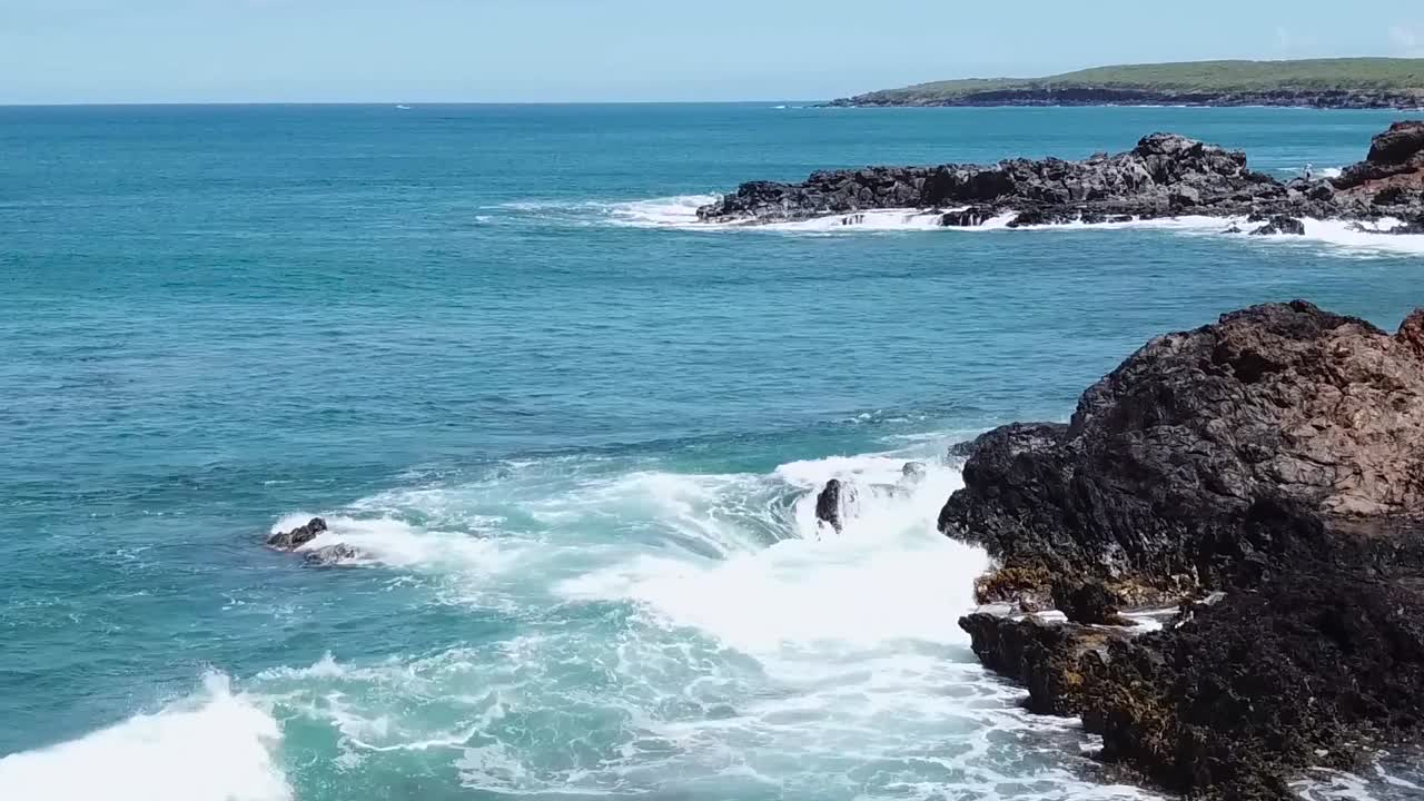 antena de drones sobre olas rompiendo en agua azul roca