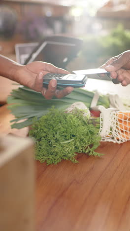 african american man's hand pays with credit card in greengrocers, vertical video, slow motion