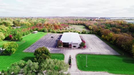 Una-Vista-De-Drone-De-Un-Gran-Almacén-Y-Un-Lote-Baldío-En-Medio-De-Un-Colorido-Follaje-De-Otoño