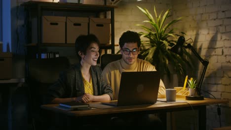 two people working on a laptop in a modern office at night