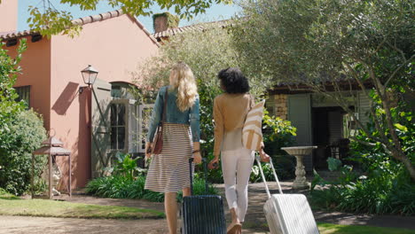 two woman friends arriving at hotel villa with trolly bags enjoying summer vacation looking at beautiful country house excited for holiday 4k footage