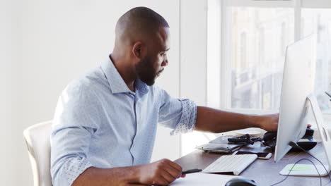 Young-black-man-using-phone-and-computer-in-office,-close-up