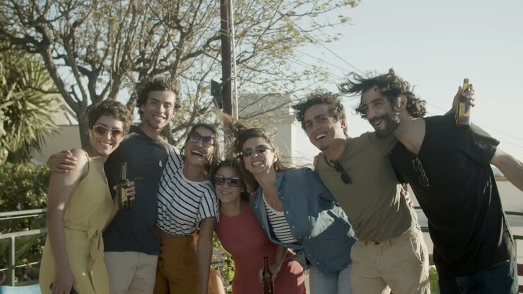 Amigos felizes se abraçando e posando para a câmera enquanto estão de pé no terraço durante uma festa ao ar livre.
