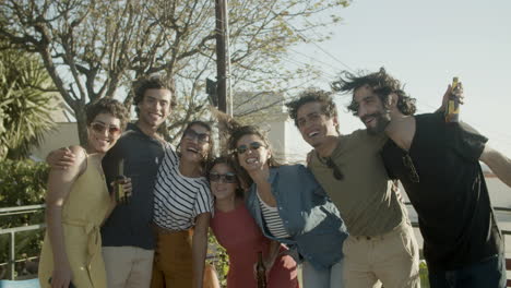 happy friends hugging and posing for the camera while standing on rooftop during an outdoor party