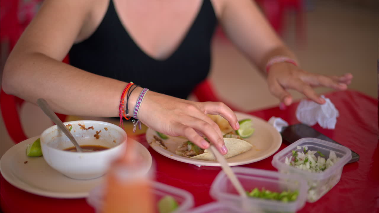 Slowmotion nærbillede af en latinamerikansk kvinde, der tilbereder sin barbacoa taco og tager en bid på en restaurant i Mexico.