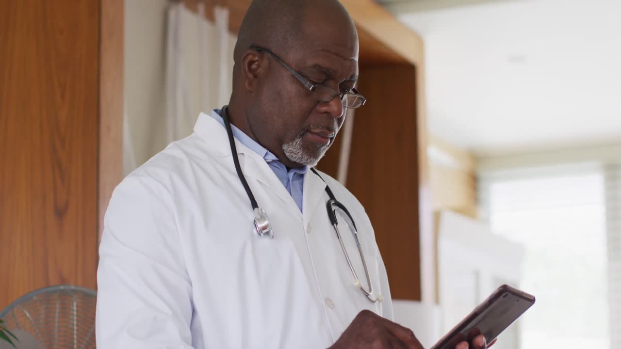 Medico anziano afroamericano con camice bianco che scrive su un quaderno.