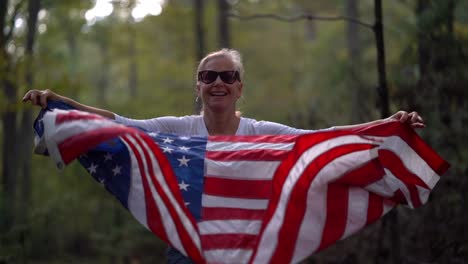 una mujer bastante madura con gafas de sol y sonriendo juega con una bandera americana agitándola hacia arriba y hacia abajo frente a ella