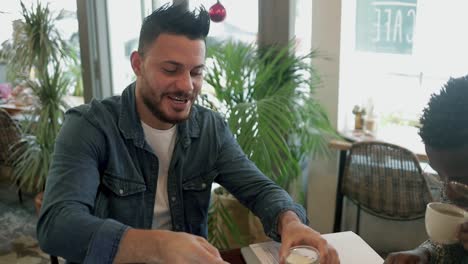 smiling man adding sugar to coffee while working in cafe