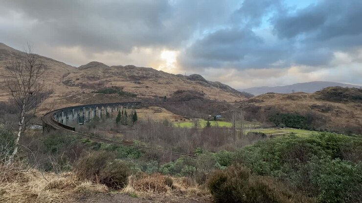 Elevated view of the Glenfinnan Viaduct in Scotland, surrounded by lush greenery and hills, cloudy sky above