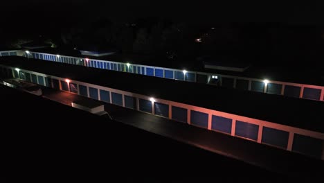 parking delivery truck and trailer in industrial zone with blue warehouse temporary storage garages at night. aerial approaching shot in virginia, usa.