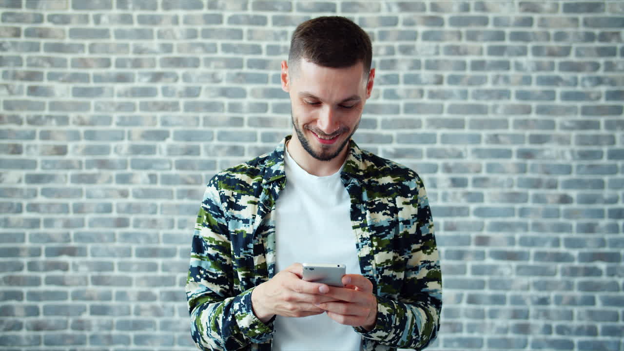 Uomo che scrive messaggi sul suo smartphone davanti a un muro di mattoni