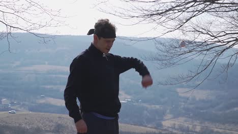a man dressed in black performs warm-up exercises in a natural outdoor setting with mountains in the background. perfect for themes of fitness, stretching, preparation, and well-being.