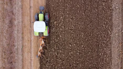 aerial view of a green plowing soil tractor driving on a farm, wide top down view