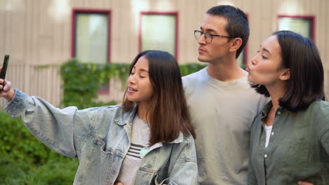 group of three young japanese friends standing outdoors and taking funny selfie photos together