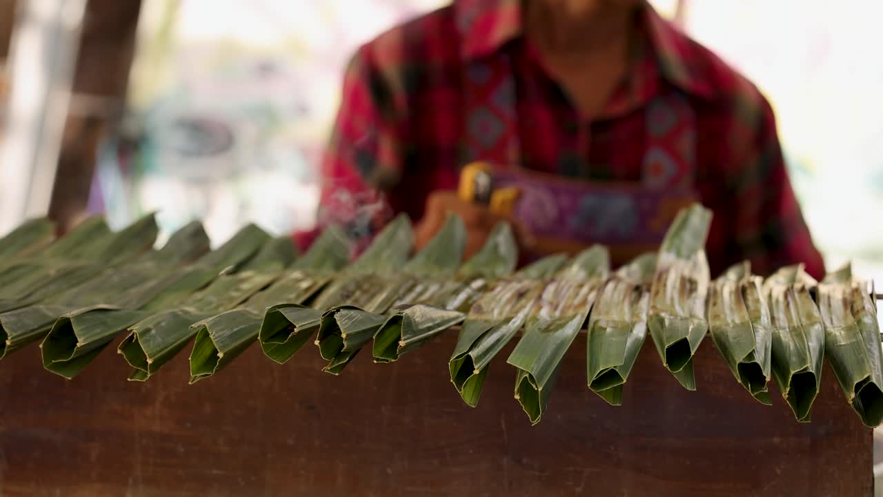 persona asando bocadillos envueltos en hojas de plátano