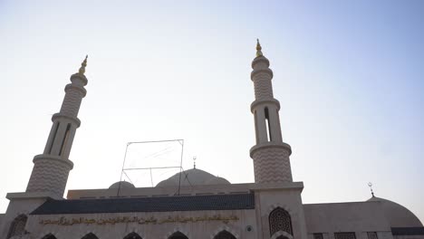 low-angle pan shot of a mosque's twin minarets rising against a clear sky, capturing its architectural details