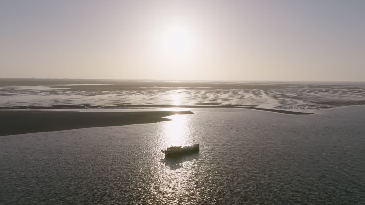 Pull in to wadden sea mudflats where a luxemotor boat sits near sandbanks with strong sun glitter