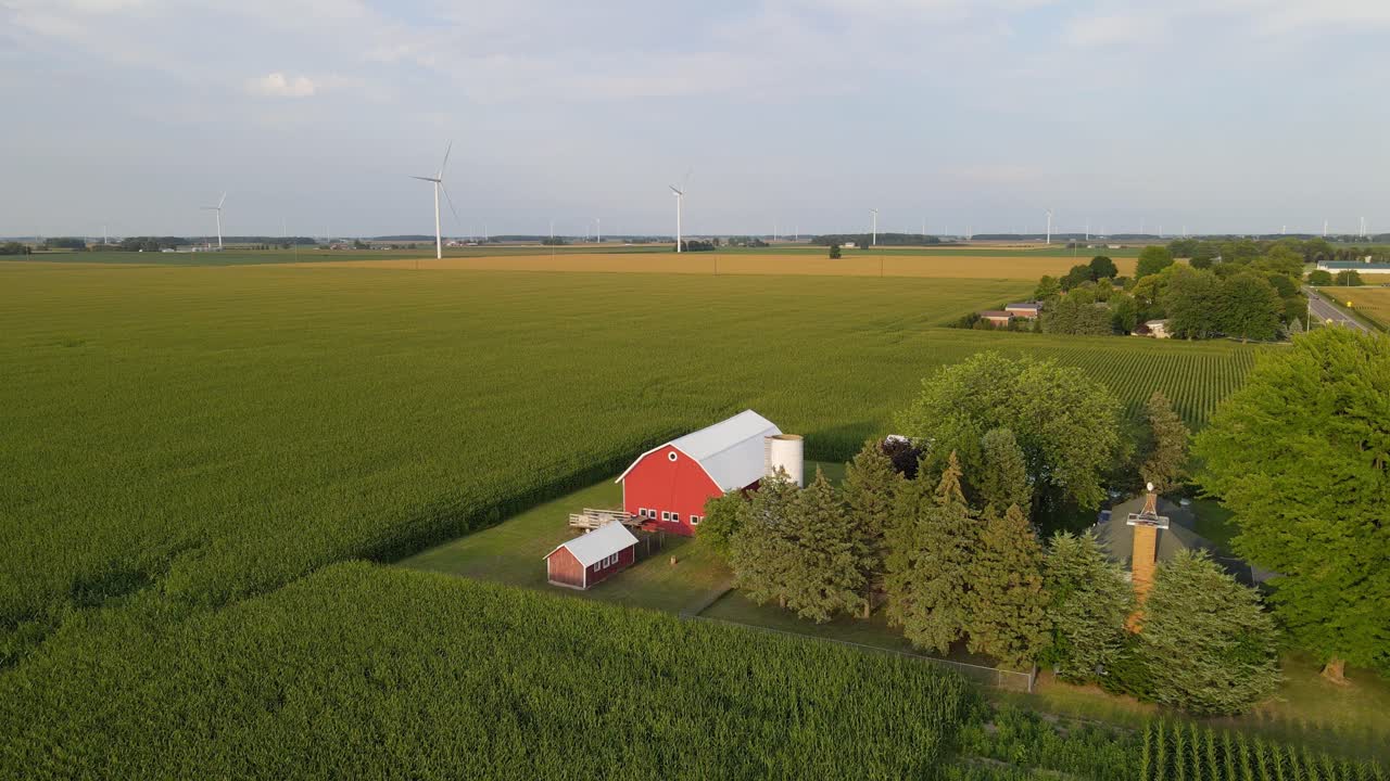 Orbiting view of a traditional farm house with a red barn and silo with wind turbines in the background